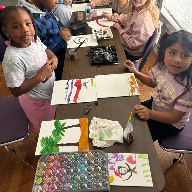 Students painting at the studio table with their artwork laid out